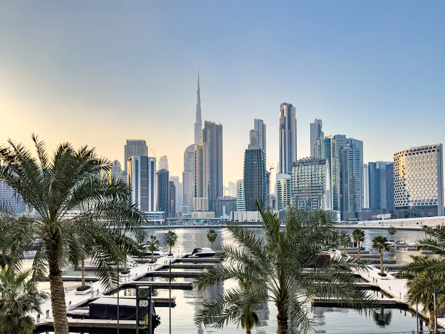 Downtown Dubai and Burj Khalifa seen across a marina lined with palm trees
